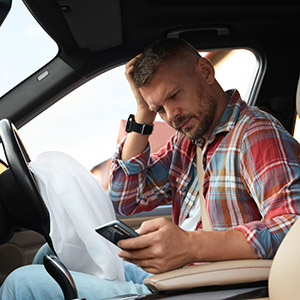 Injured man using smartphone near opened airbag in automobile after car accident